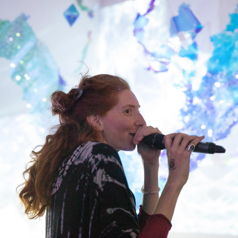 Martina Mrongovius speaking into a microphone at the opening of SPACE:LIGHT. photo by Wen Han-Chan, artwork by Julia Sinelnikova SPACE:LIGHT, 2019