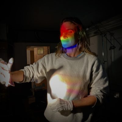 Chrissy Stuart During the Southwood Holographic Artist in Residence | the artist's face is illumaunted by a raibow created by the hologram - diffrection grating, that she is holding.