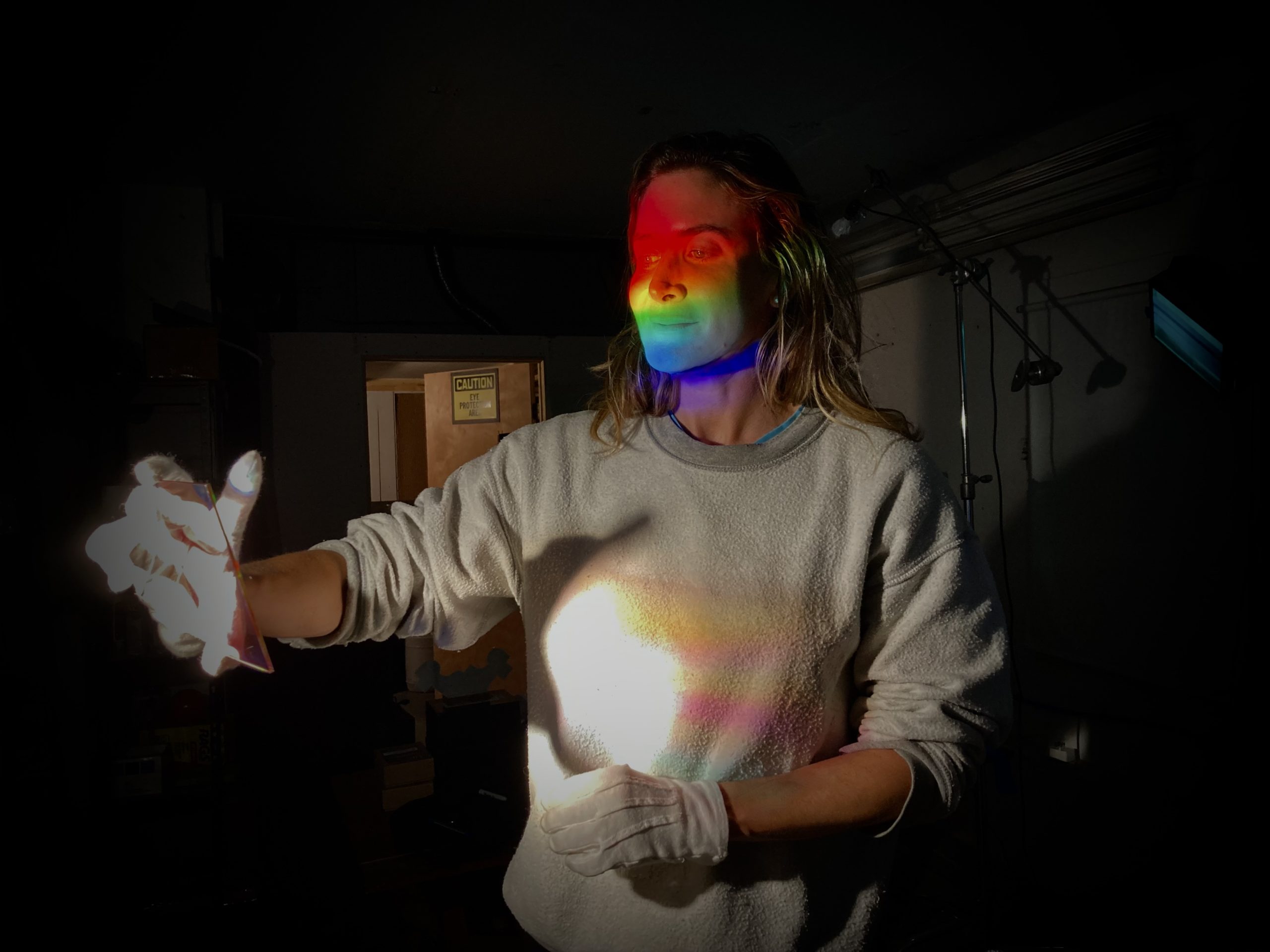 Chrissy Stuart During the Southwood Holographic Artist in Residence | the artist's face is illumaunted by a raibow created by the hologram - diffrection grating, that she is holding.